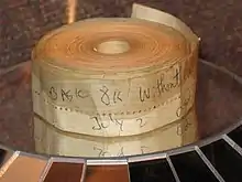 An aged roll of paper tape perhaps 1–2 inches (2.5–5.1 cm) wide; on the outside is written "BASIC 8K without cassette" and "July 2" in blue biro pen.