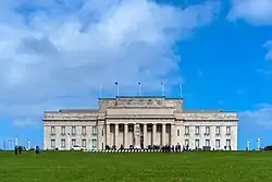 Large neoclassical-style building with a forecourt featuring a Cenotaph on a Court of Honour. Above the front porch of the building is inscribed a funeral oration attributed to the Greek General Pericles, which reads "MCMXIV&nbsp;– MCMXVIII / The whole earth is the sepulchre of famous men / They are commemorated not only by columns and inscriptions in their own country / but in foreign lands also; by memorials graven not on stone / but on the hearts of men." A New Zealand flag atop the building is flown at half-mast. Banners hanging between the columns advertise exhibitions about volcanoes, and Charles Darwin.