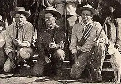 Photo taken in 1893 of three Bulawayo field scouts kneeling in front of their horses. Bob Bain on the left, Burnham in the middle, Maurice Gifford and his dog on the right. Burnham is dressed in his Arizona clothes and is holding his Winchester model 1873 .44WCF rifle