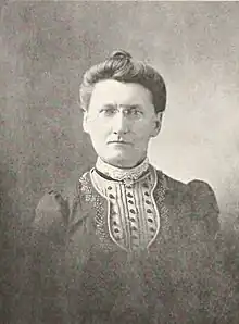 B&W portrait photo of a middle-aged woman with her hair in an up-do, wearing a dark blouse with a frilly front.