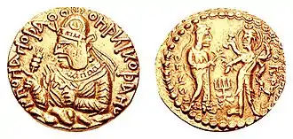 Coin of Huvishka with the divine couple Ommo ("ΟΜΜΟ", Umā) holding a flower, and Oesho ("ΟΗϷΟ", Shiva) with four arms holding attributes. c. 150-180 CE.
