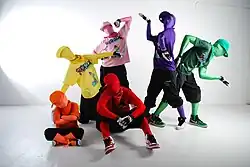 People wearing vibrant zentai suits with matching T-shirts and caps posing in a white room
