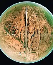 An aerial view, looking east, over Forrest using a fish-eye lens. The entire view, other than a railway line, a train on it, and some houses and sidings, is low desert scrub.