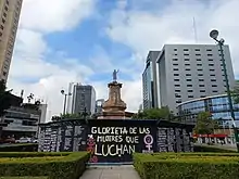 A sculpture of a woman raising her fist in the air lies on a plinth.