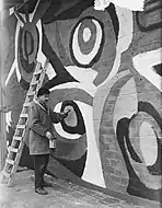 Karel Appel, 1955: Karel Appel is painting on the wall of an exposition-building in Rotterdam - photo, 19 April 1955 by Joop van Bilsen / Anefo - National Dutch Archive