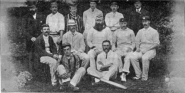 11 men dressed in cricket clothing posing for a group photograph. Three rows.