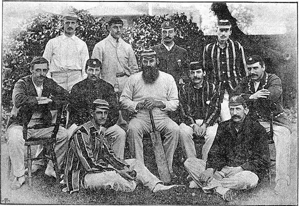 11 men dressed in cricket clothing posing for a group photograph. Three rows.