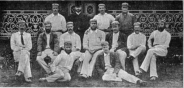 13 men dressed in cricket clothing posing for a group photograph. Three rows.